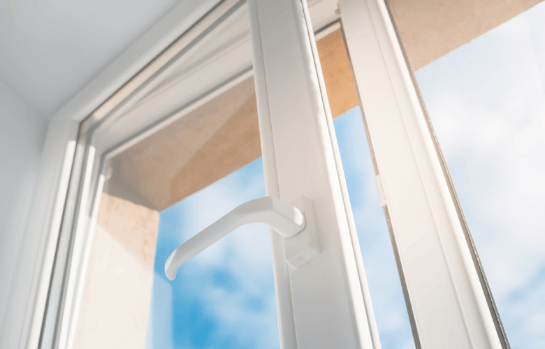 Een raam van witte PVC-ramen staat een beetje open op een zonnige dag met een blauwe hemel.