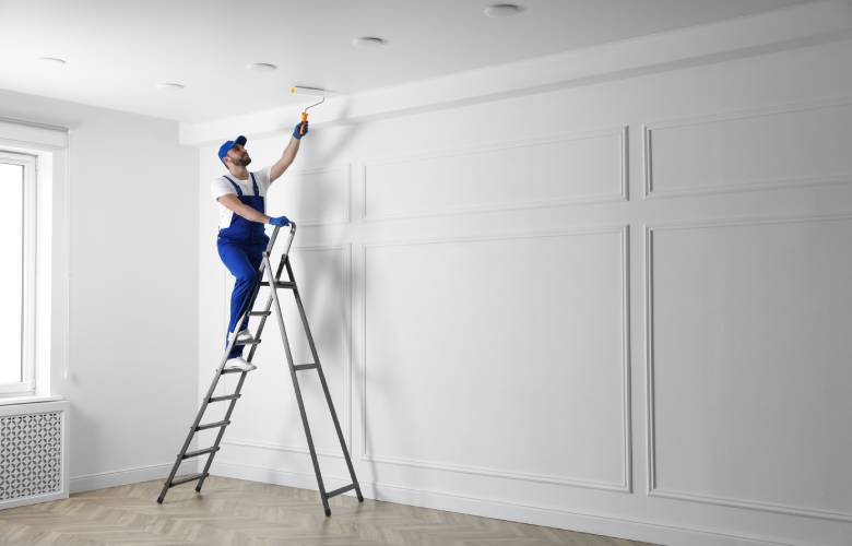 Een schilder staat op een ladder en is het plafond aan het schilderen.
