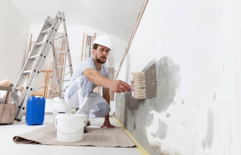 Een professionele schilder die een muur aan het schilderen is met al zijn materiaal op de achtergrond.