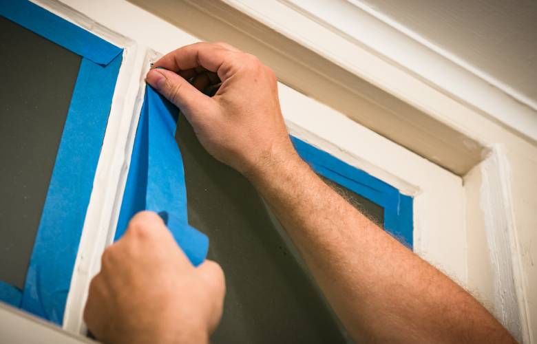 Een persoon is een raam aan het tapen om het te gaan schilderen.